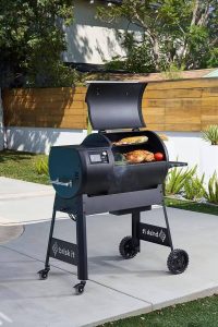 Brisk It Origin-580 black pellet grill on an outdoor patio, featuring a digital control panel, hood open, wheels and Brisk It branding for a modern, durable cooking setup